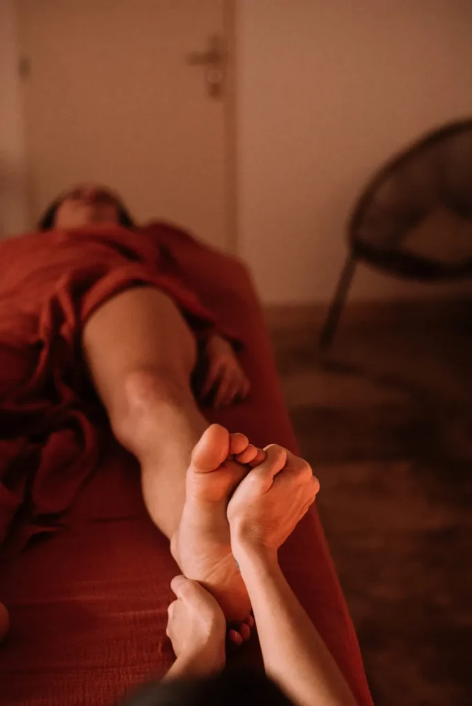 Massage des pieds en fin de soin, cliente allongée sous un drap terracotta